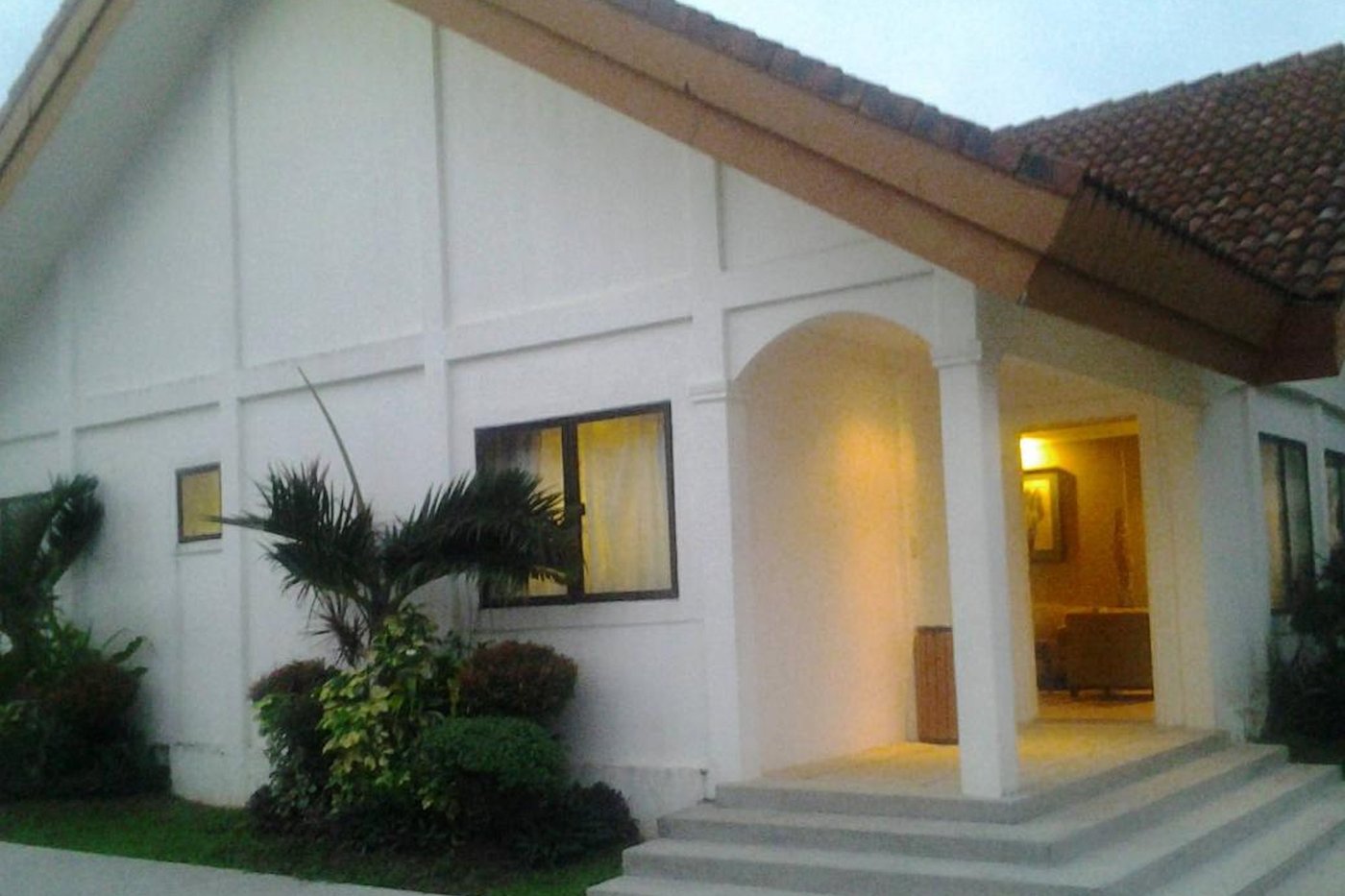 A white villa with red-tiled roof under a warm porch light